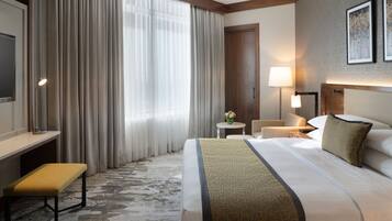 Habitación de hotel con una cama grande, un escritorio, una silla, una lámpara y una mesita con un jarrón de flores.