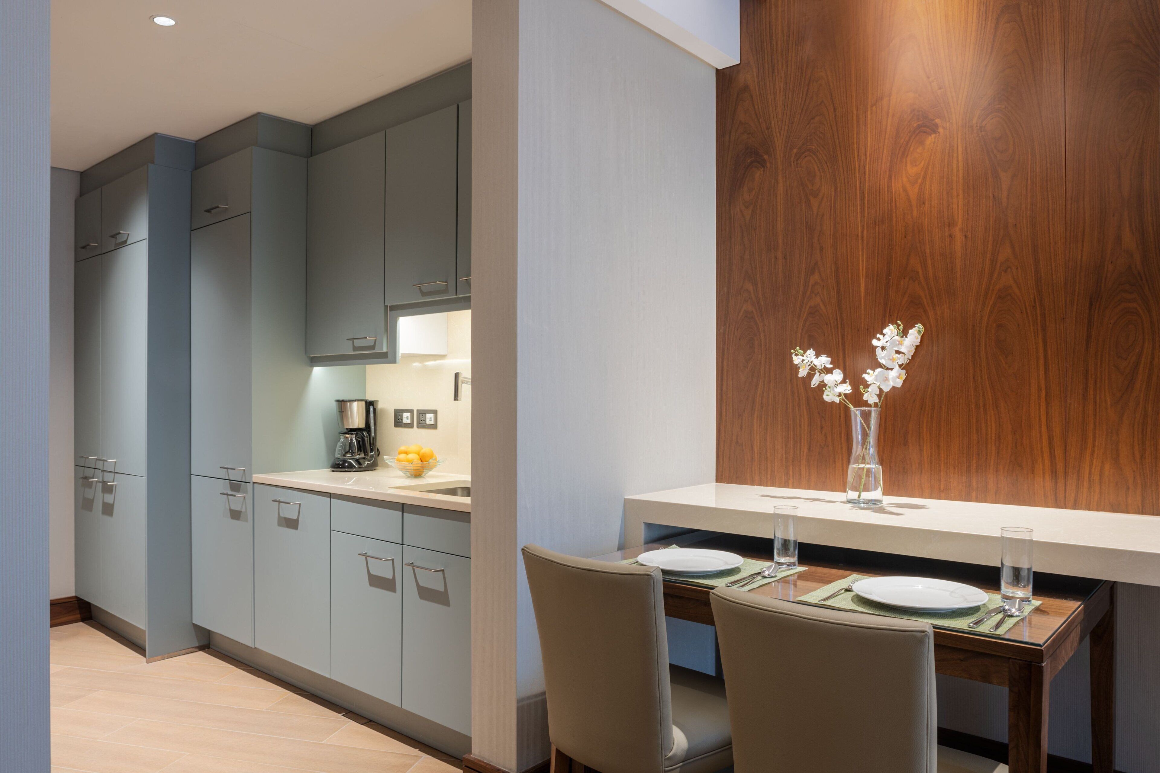 A modern kitchen with grey cabinets, a wooden accent wall, and a dining area with a table set for two.