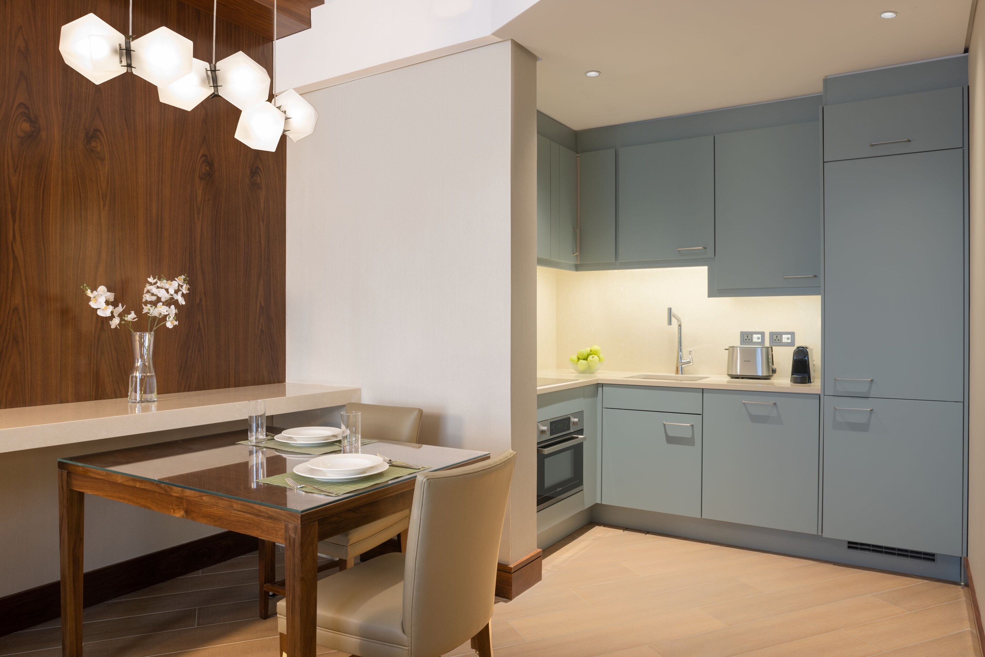 A modern kitchen with light blue cabinets, a wooden dining table, and a hanging light fixture.