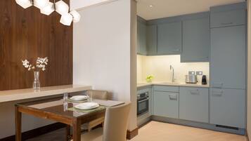 A modern kitchen with light blue cabinets, a wooden dining table, and a hanging light fixture.
