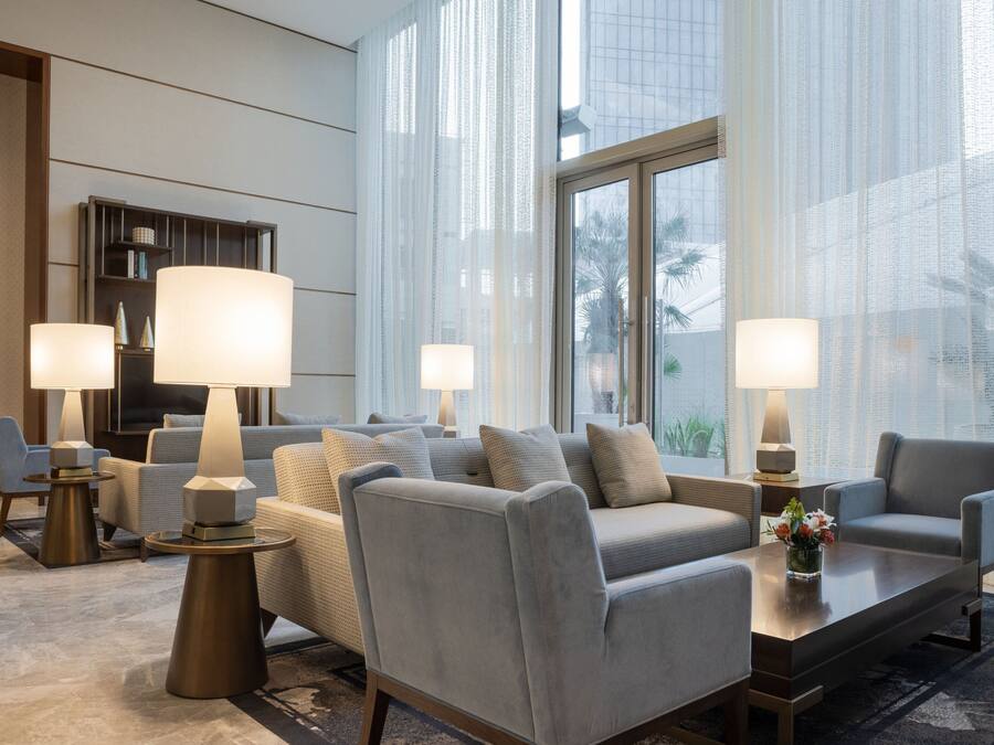 Un moderno vestíbulo de hotel con un área de descanso, ventanas amplias y una estantería.