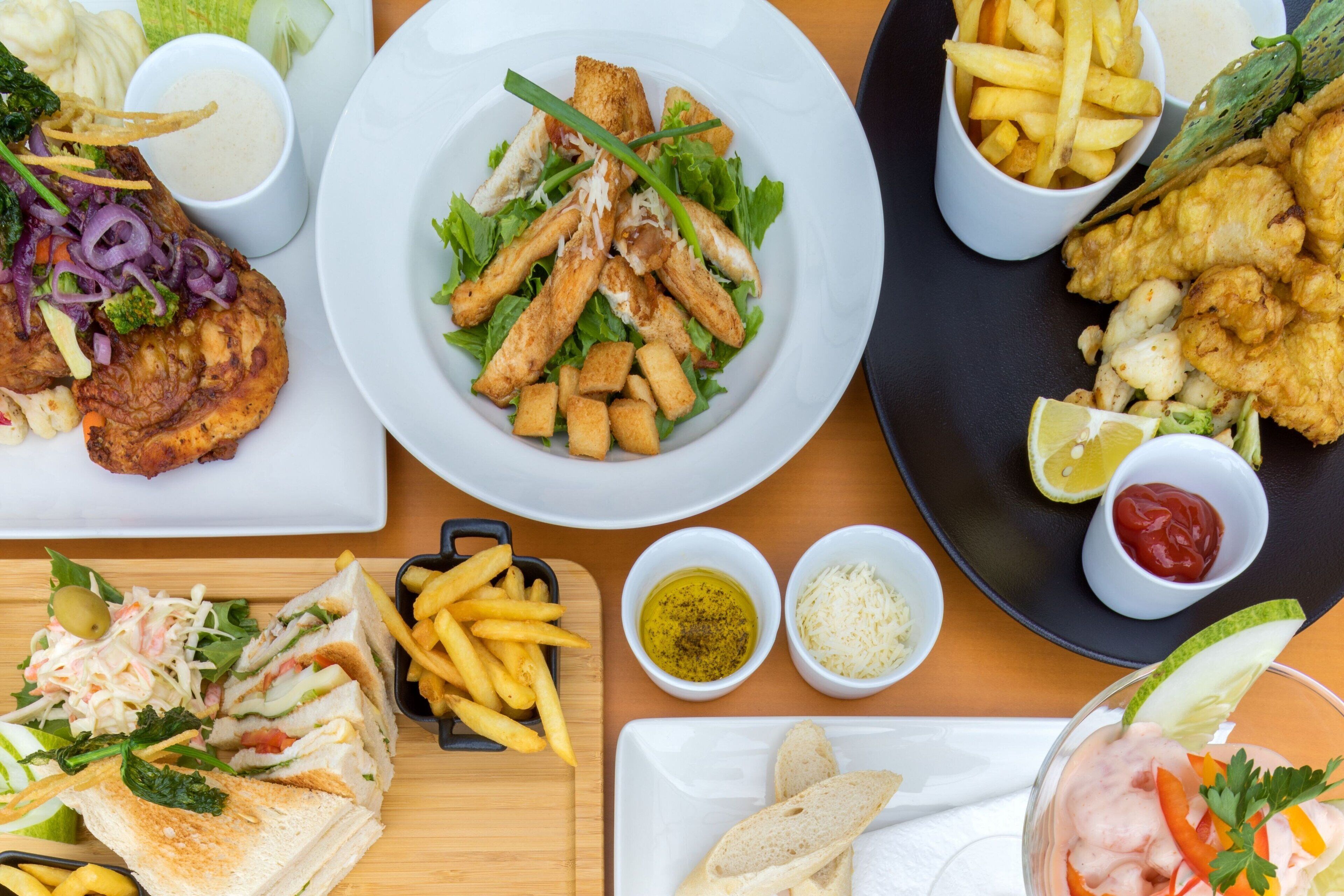 A variety of dishes including a sandwich, fries, and fried items, served on multiple plates.