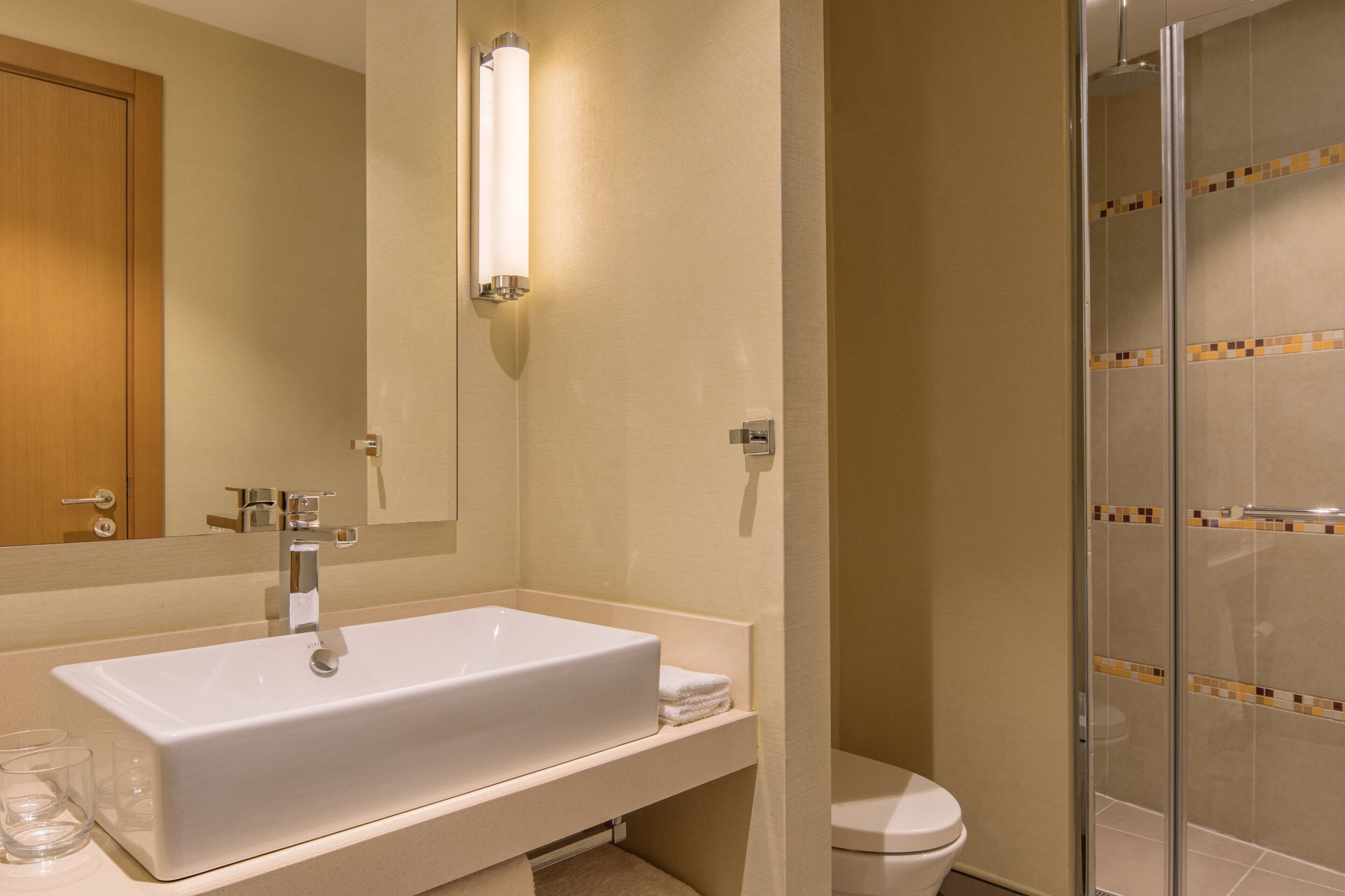 Een moderne badkamer met een wit wastafelmeubel, een spiegel, een douchecabine van glas en een toilet.