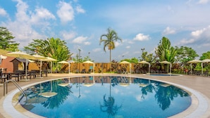 A swimming pool with lounge chairs and umbrellas, surrounded by palm trees and greenery. - Four Points By Sheraton Ikot Ekpene (Ikot Ekpene)