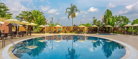 A swimming pool with lounge chairs and umbrellas, surrounded by palm trees and greenery.