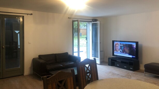 Ett vardagsrum med en svart lädersoffa, ett matbord i trä och en tv.