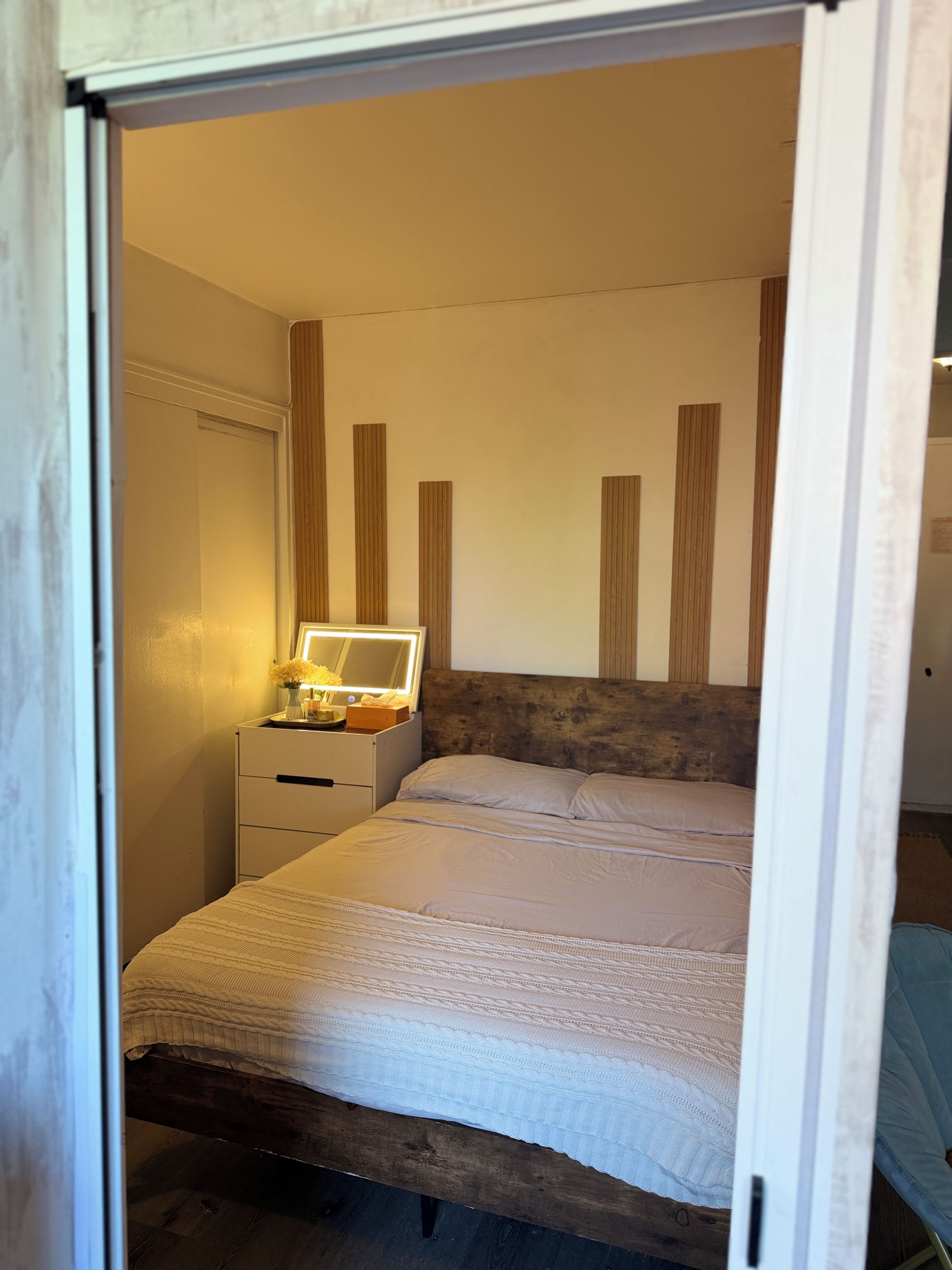 A bedroom with a bed, a bedside table with a lamp, and a mirror.