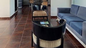 Un vestíbulo moderno con piso de baldosas oscuras, un sofá azul y una mesa de recepción.