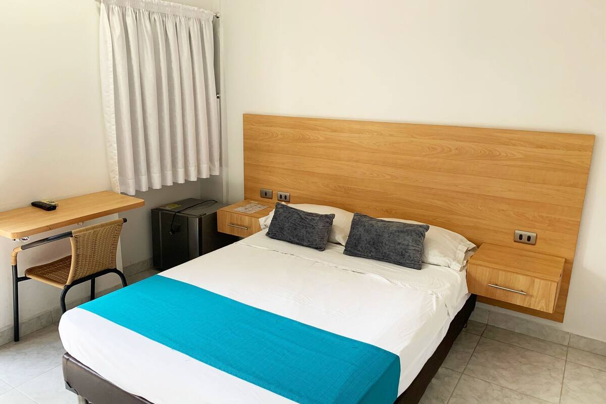 A hotel room with a bed, a desk, a chair, a nightstand, and a small cabinet.