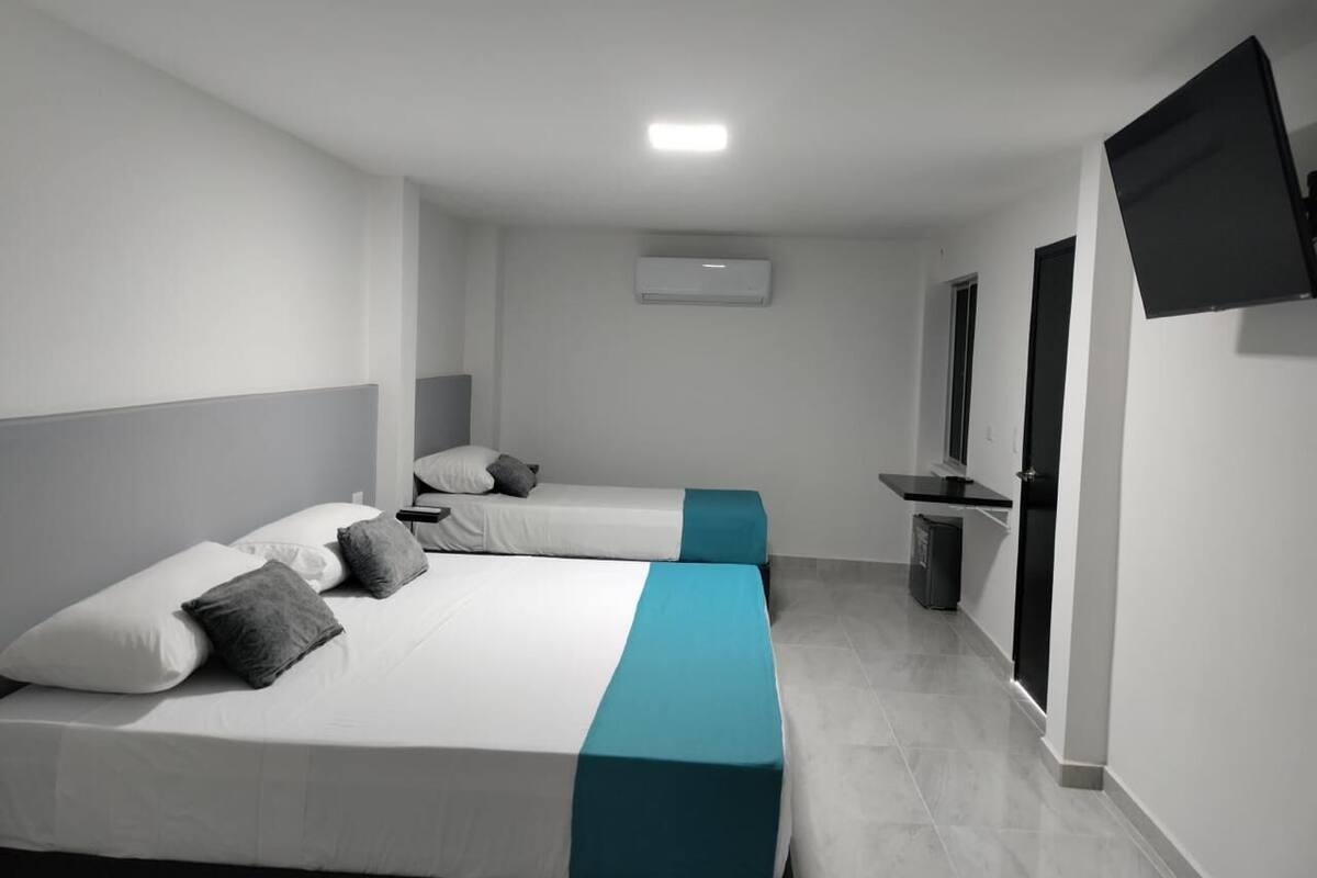 A hotel room with two beds, a TV mounted on the wall, and a small desk area.