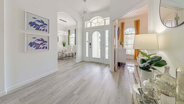 Un hall d’entrée spacieux, doté d’un plancher en bois, d’une porte blanche et d’un miroir sur le côté droit.