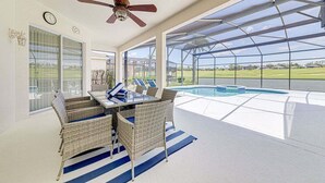 Une terrasse couverte avec une piscine, des meubles en osier et un ventilateur de plafond.