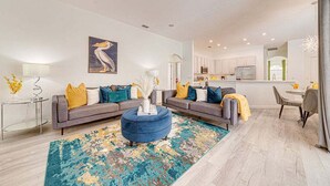 Un salon moderne avec un canapé gris, un pouf bleu et un tapis coloré.