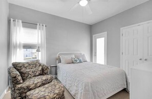 A bedroom with a bed, a chair, a ceiling fan, and a door.
