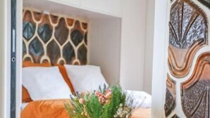 Una habitación con una cama, una mesita de madera con un jarrón de flores y un panel decorativo en la pared.
