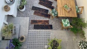 Un patio con una mesa y sillas de madera, rodeado de macetas con plantas y leños decorativos.