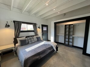 Makuuhuoneessa on sänky, penkki, vaatekaappi ja ikkuna, jossa on verhot.