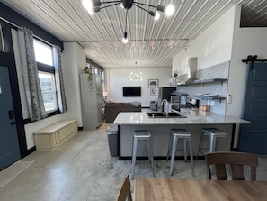 Ett modernt kök med en central köksö, vitvaror i rostfritt stål och en matplats med ett träbord och stolar.