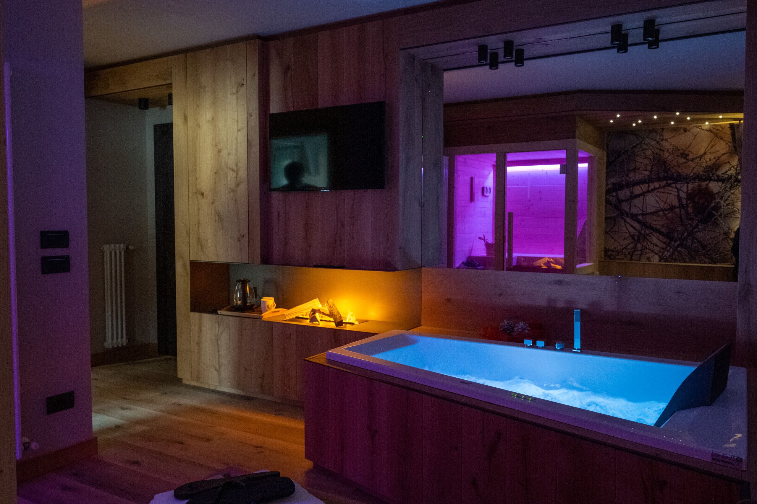 Un bagno moderno con un mobile lavabo in legno, una vasca da bagno ampia e una TV fissata alla parete.