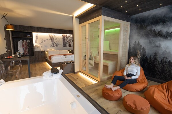 A modern hotel room with a large bathtub, a seating area with orange bean bags, and a mural of a forest.