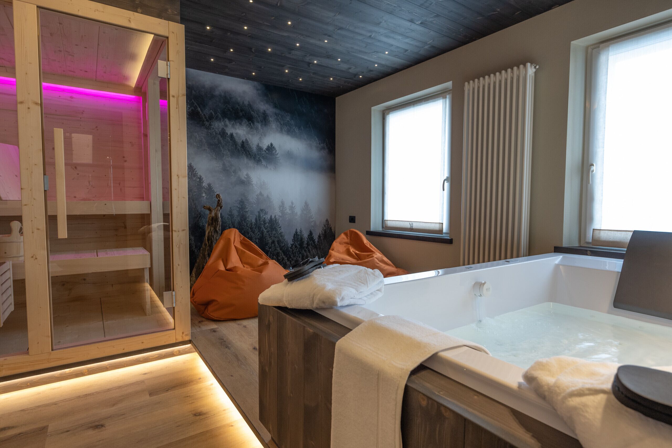 A spa room with a wooden bath, a massage table, and a wall mural of a forest.