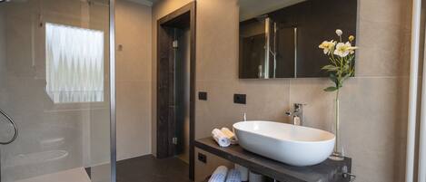 A modern bathroom with a glass shower enclosure, a large white sink, and a mirror above it.