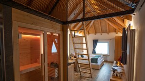 Una cabaña de madera con habitación en el altillo, baño con ducha y zona de cocina.