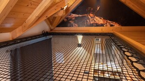 Una habitación con techo de madera inclinado, piso de malla metálica y vista a un paisaje rocoso a través de un ventanal triangular.