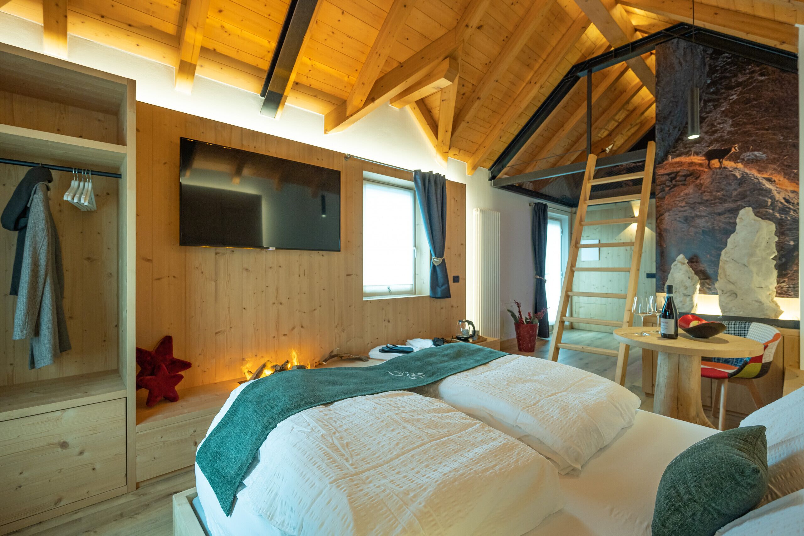 A cozy bedroom with a wooden ceiling, a bed with white linens, a mounted TV, and a stone wall feature.