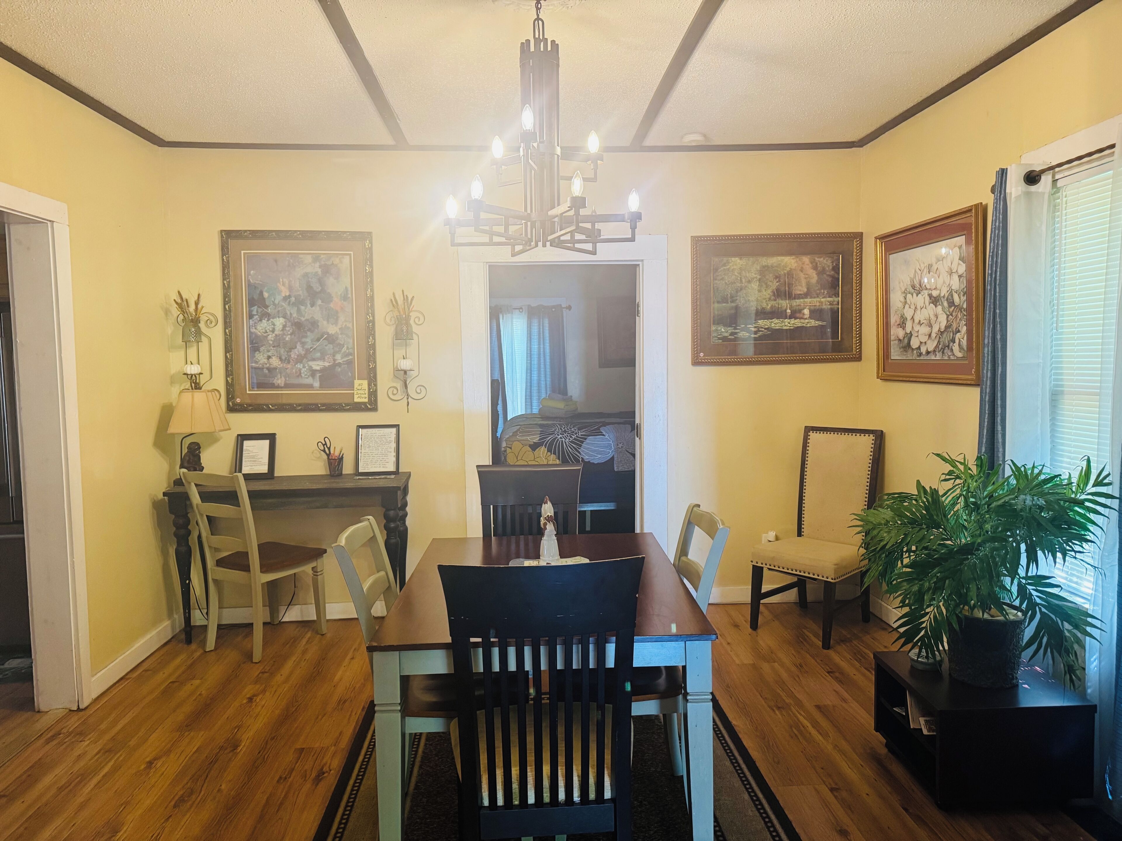 A dining room with a wooden table, chairs, a chandelier, and framed artwork on the walls.
