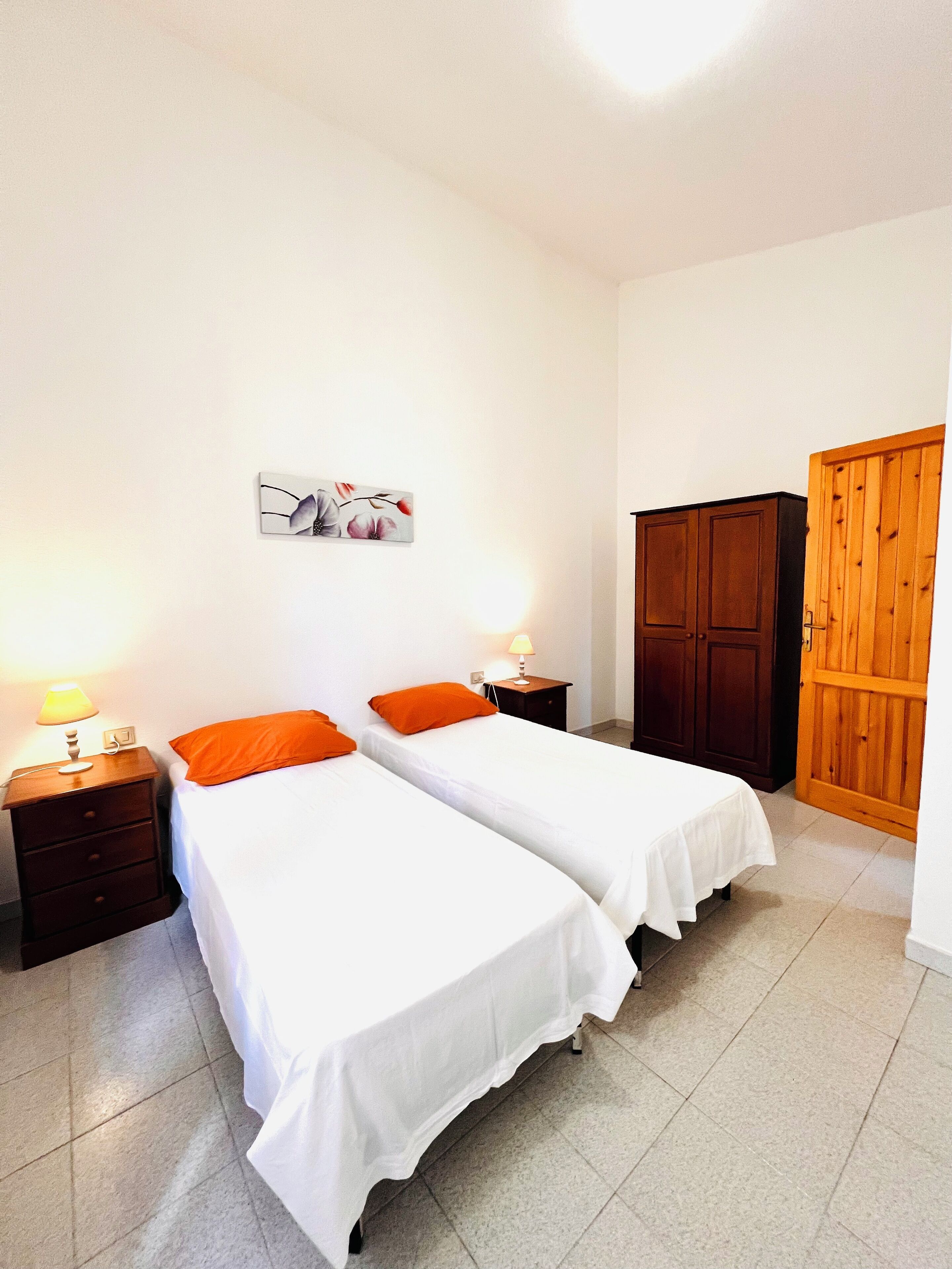 Quarto com duas camas de solteiro, um guarda-roupa de madeira, uma mesa de cabeceira com abajur e um quadro na parede.