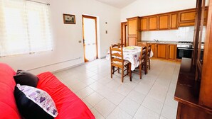 Ett kompakt bostadsutrymme med matplats, kök och en röd soffa.
