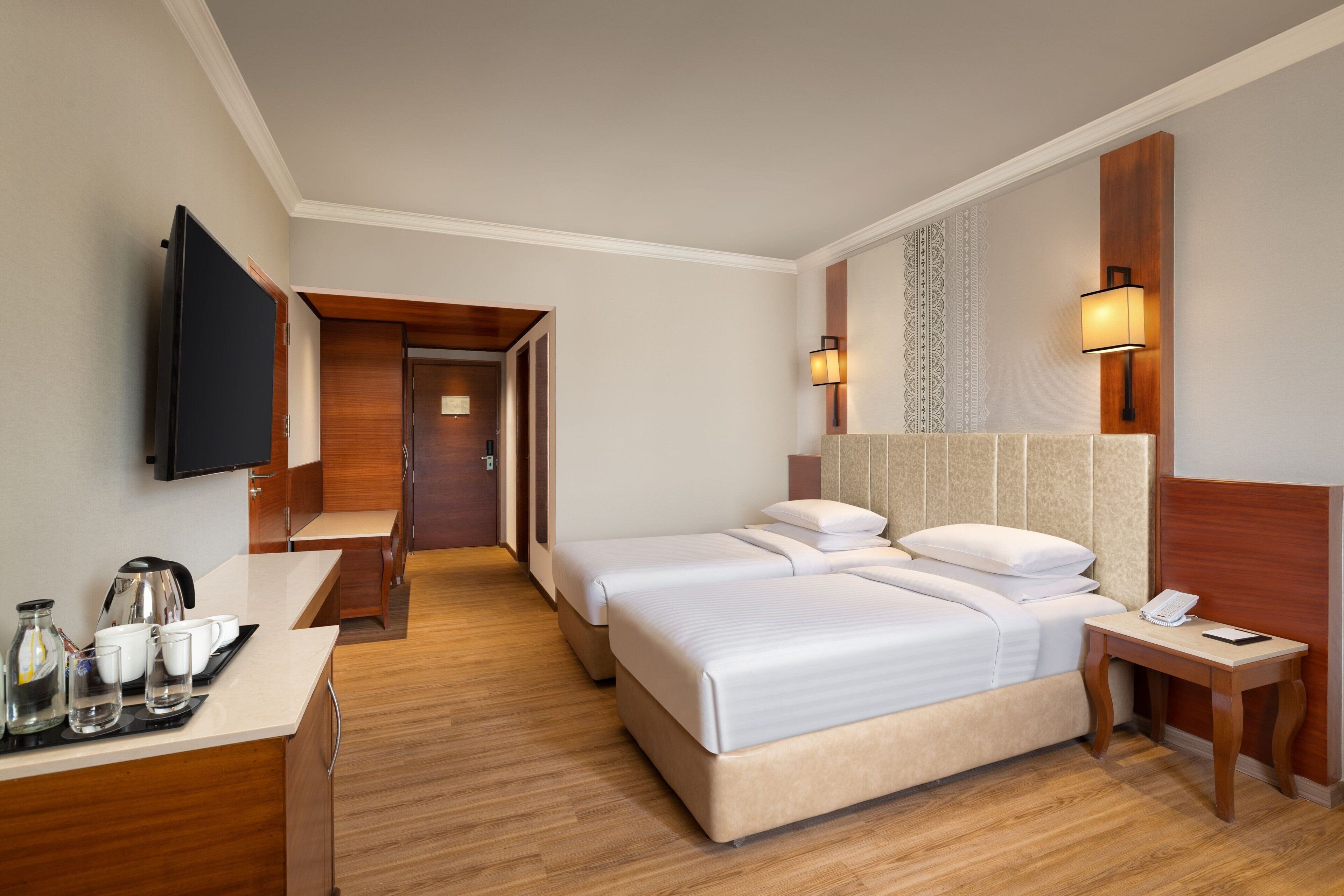 Habitación de hotel con dos camas, televisión, escritorio con cafetera y mesita de noche con teléfono.