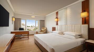A hotel room with a large bed, a desk, a chair, and a television.