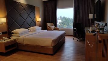 Una habitación de hotel con una cama grande, un escritorio con teléfono, una silla, televisión y una ventana con cortinas.
