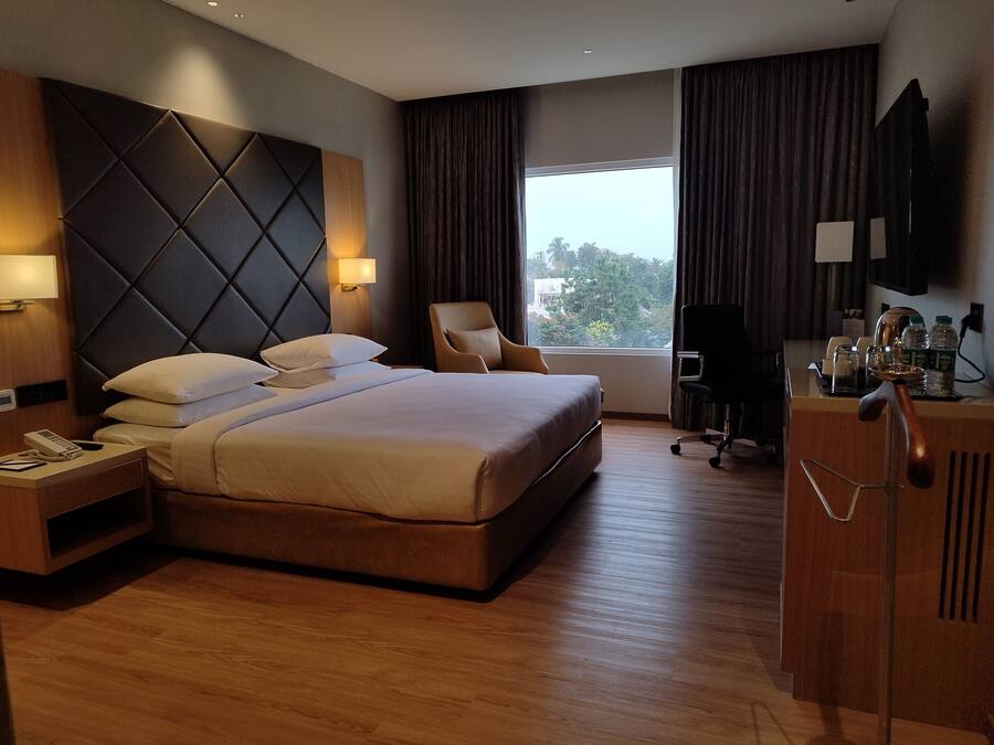 Una habitación de hotel con una cama grande, un escritorio con teléfono, una silla, televisión y una ventana con cortinas.