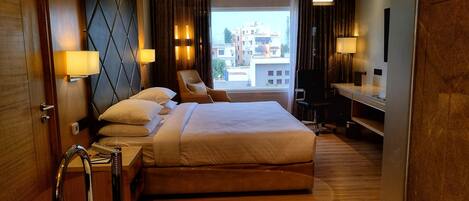 Une chambre d’hôtel avec un grand lit, un bureau, une chaise et une vue sur la ville par la fenêtre.