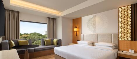 Habitación de hotel con una cama grande, un sofá, una mesa de comedor y vistas a zonas verdes.