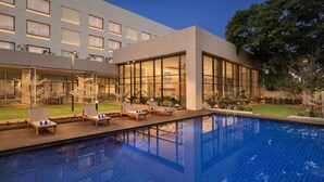 A modern hotel with a swimming pool, lounge chairs, and a well-maintained garden.