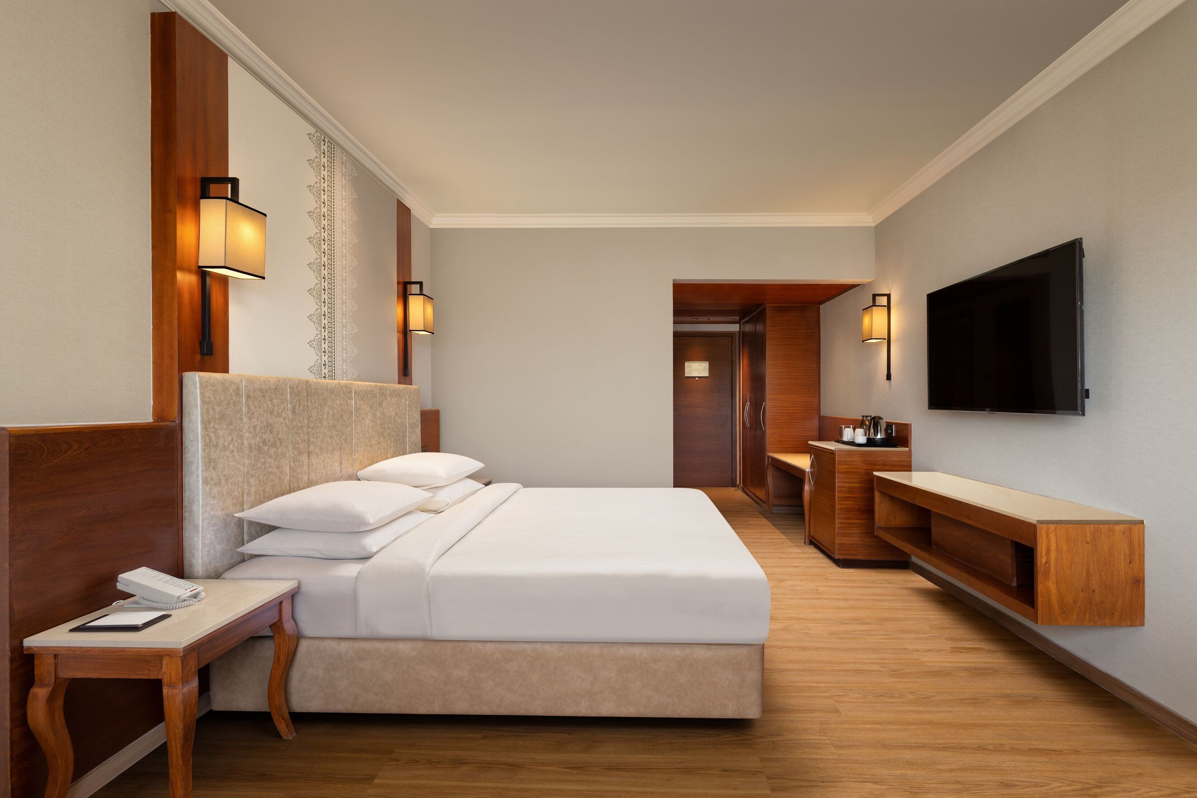 Ein Hotelzimmer mit einem großen Bett, Nachttischen, einem an der Wand befestigten Fernseher und einer hölzernen Bank.