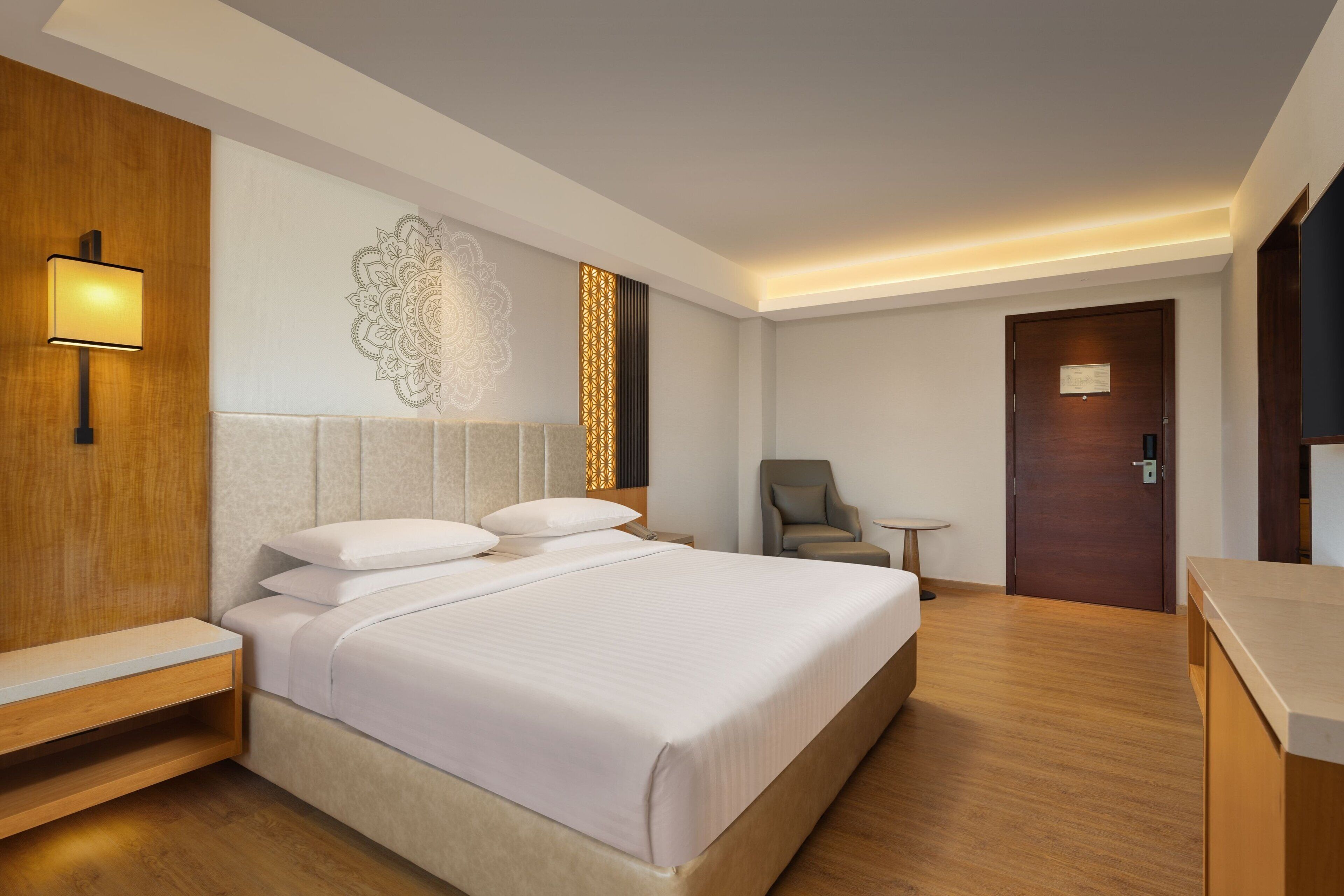 A hotel room with a large bed, bedside tables, a chair, a small table, and a door.
