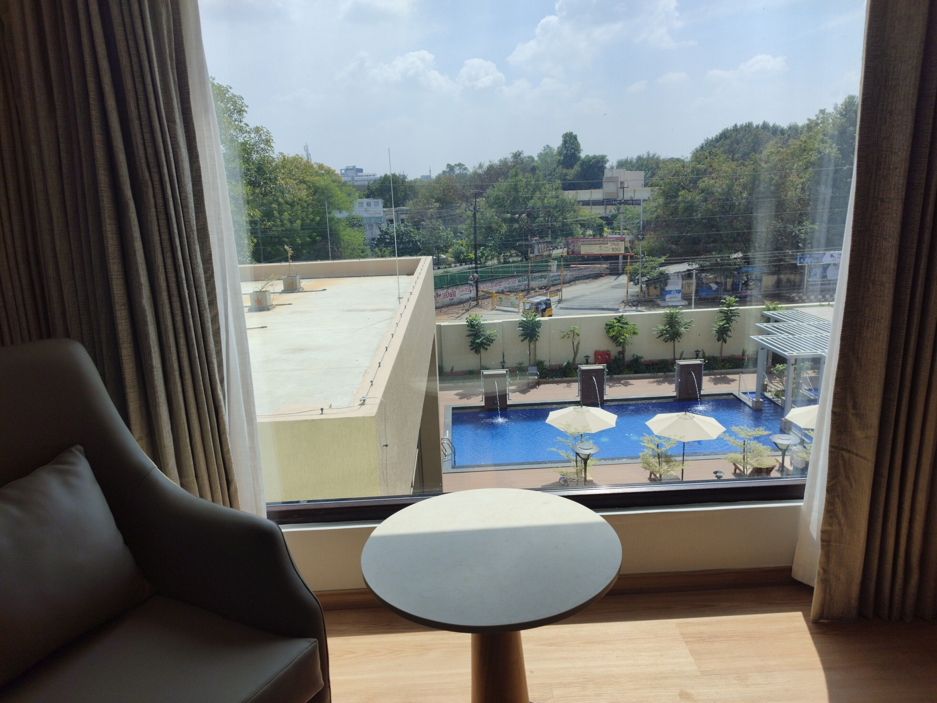 A room with a view of a rooftop pool area, a chair, and a small table.