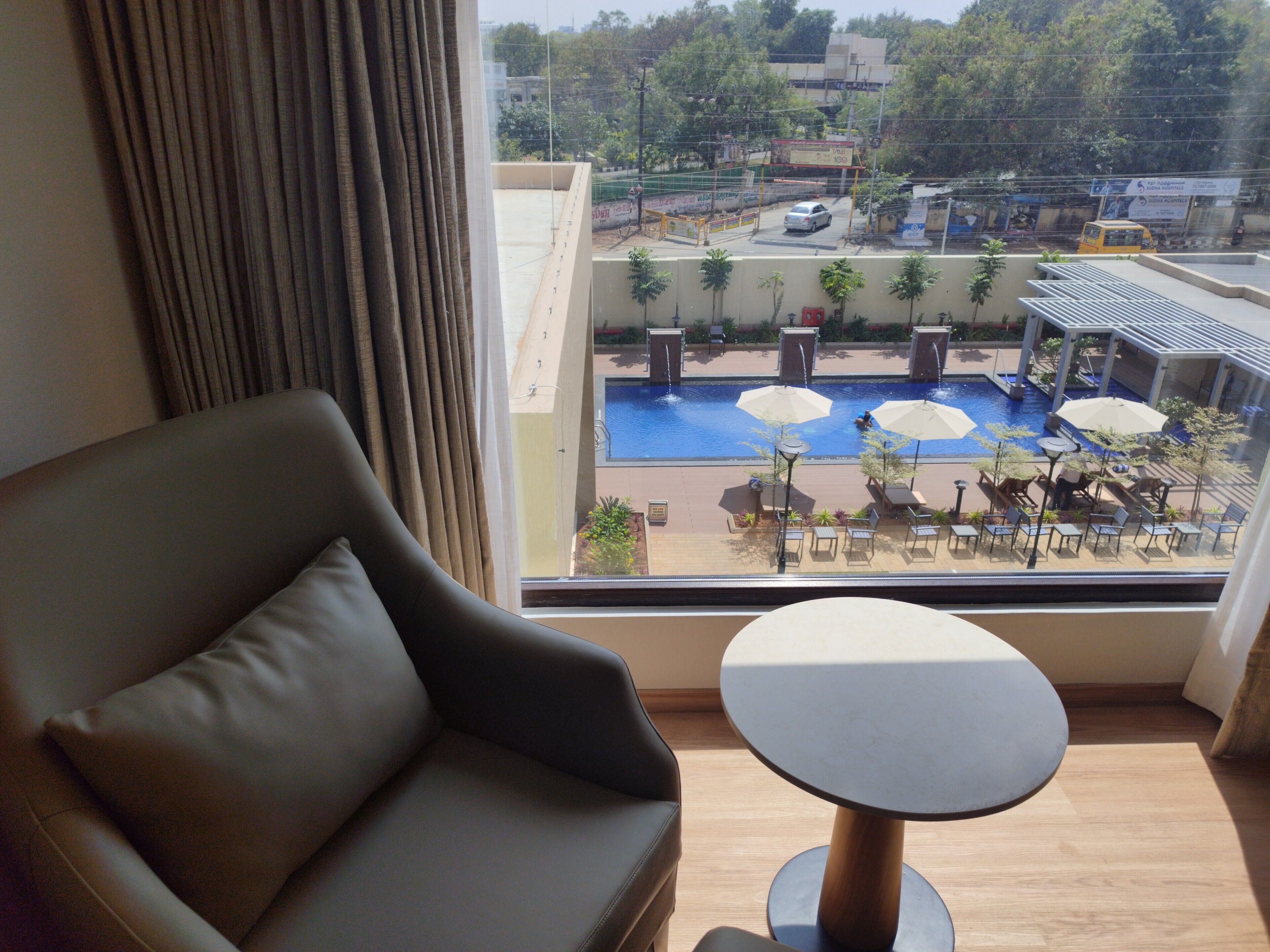 A hotel room with a view of an outdoor swimming pool, a sofa, and a small table.