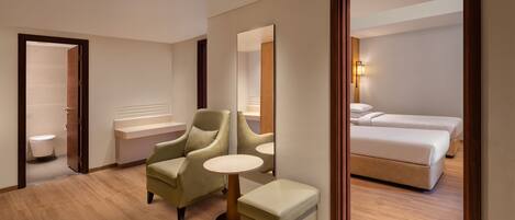 Habitación de hotel con piso de madera, sofá, una mesita redonda, cama y baño visible a través de una puerta abierta.