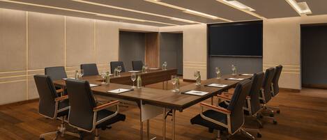 A conference room with a long table, chairs, and a projector screen.