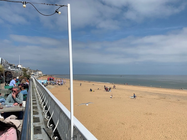 A beach with a promenade, people, and a clear sky.