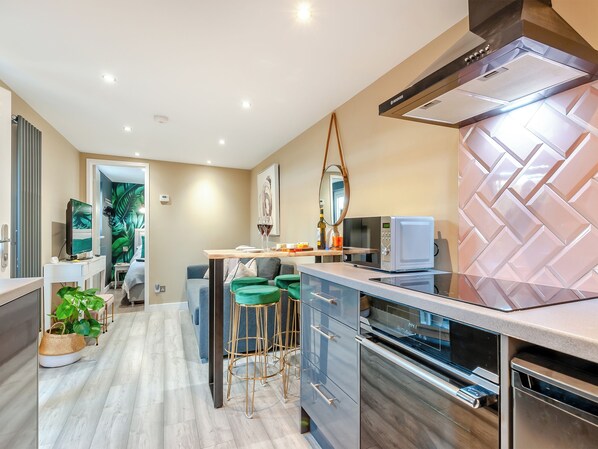 Een moderne keuken met een magnetron, oven en een geïntegreerde afzuigkap. Er is een eethoek met een tafel en stoelen.