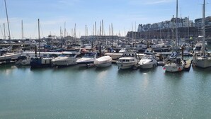 Un port de plaisance où sont amarrés de nombreux bateaux, un ciel dégagé et des bâtiments en arrière-plan.
