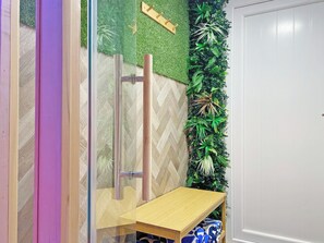 Ein Badezimmer mit Duschkabine aus Glas, einer Holzbank und einer wandmontierten Pflanzenausstellung.