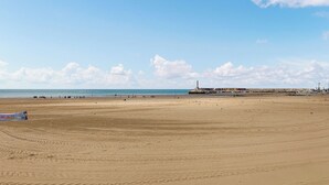 Une vaste plage de sable où l’on peut voir des empreintes, un phare situé au loin et une jetée bordée de bâtiments.
